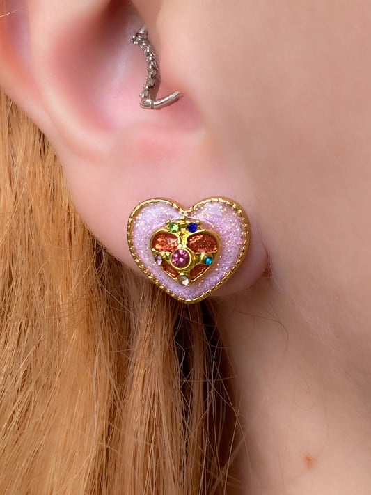 Close-up of a pink glitter heart-shaped earring worn by a person with blonde hair.
