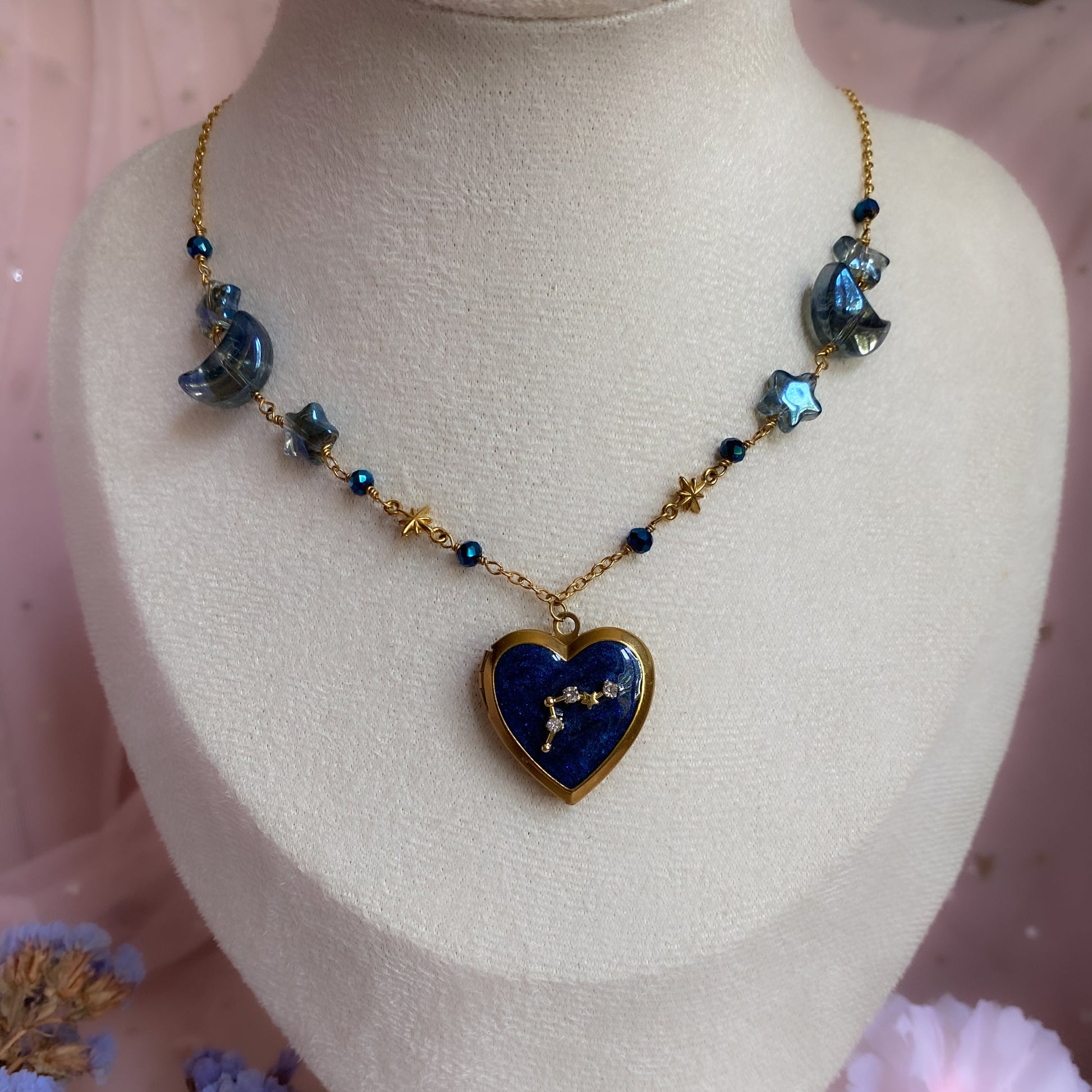 Necklace with a heart-shaped blue pendant on a mannequin bust with flowers in the background