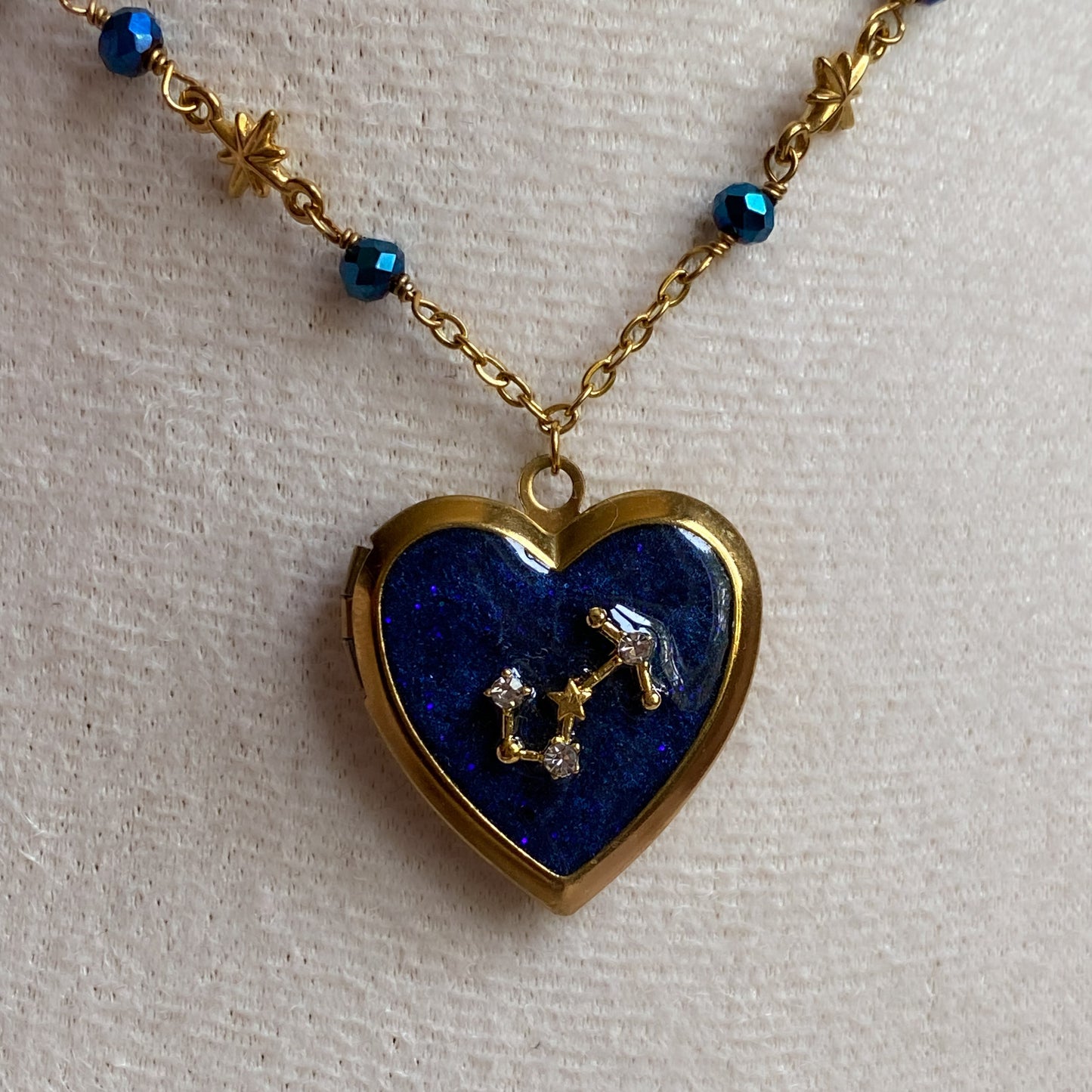 Heart-shaped locket with blue stone and star design on a gold chain against a light background