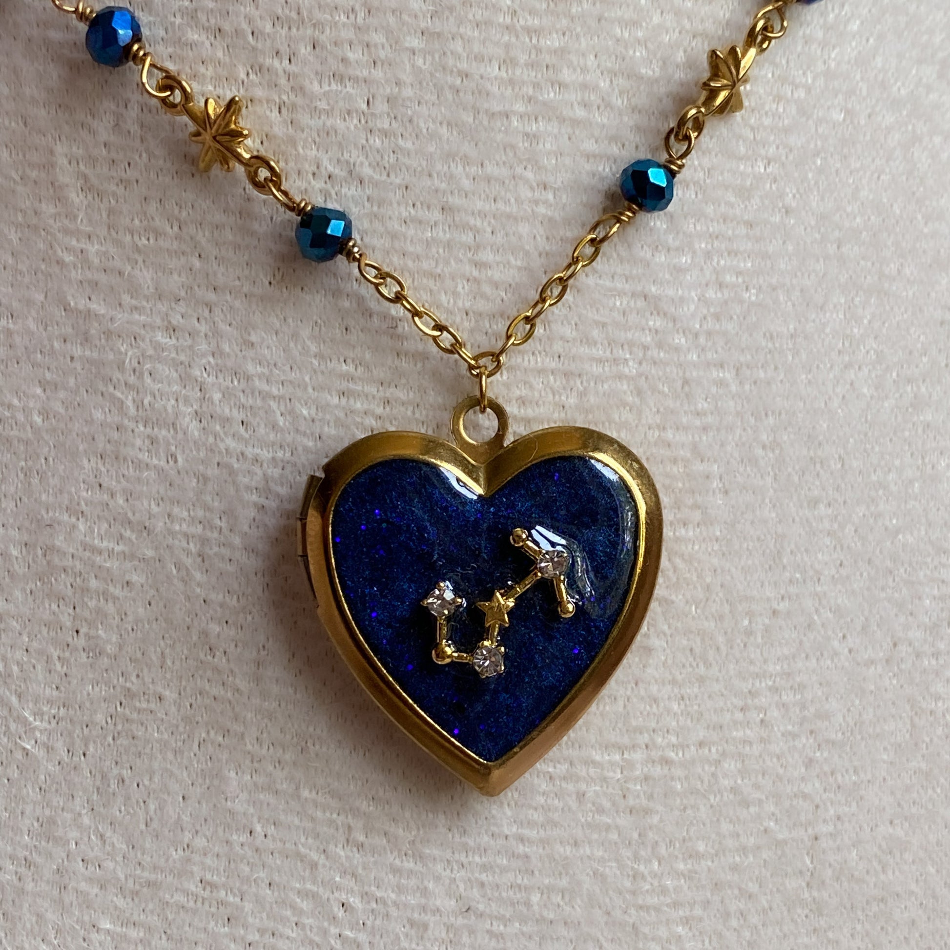 Heart-shaped locket with blue stone and star design on a gold chain against a light background