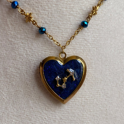 Heart-shaped locket with blue stone and star design on a gold chain against a light background