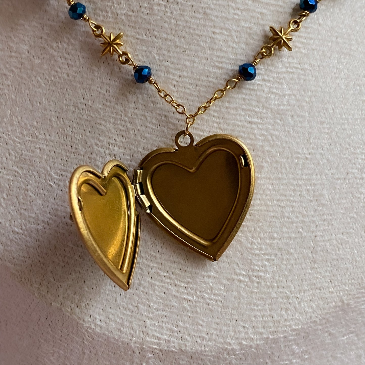 Gold heart-shaped locket on a chain with blue beads against a light background